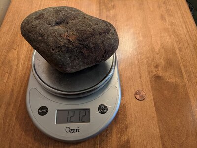 A cobble sized rock showing that it weighs 1212 grams